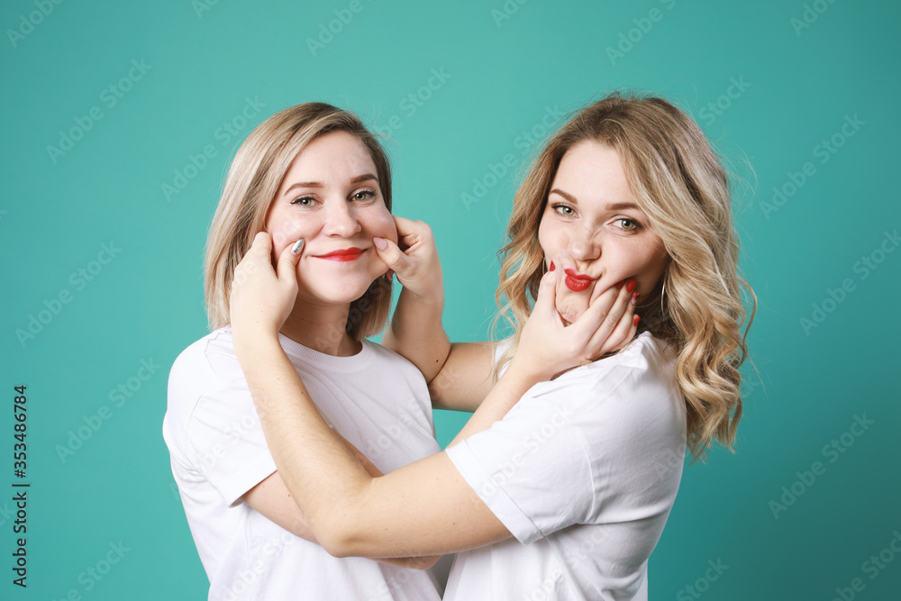 Portrait of cute twins blondes grimace each other isolated on green background Portrait of cute twins blondes grimace each other isolated on green background