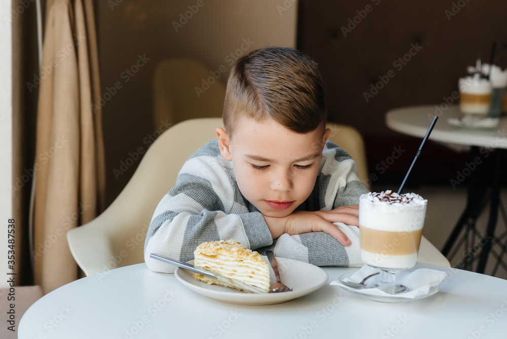 A cute little boy is sitting in a cafe and looking at a cake and cocoa close-up. Diet and proper nutrition A cute little boy is sitting in a cafe and looking at a cake and cocoa close-up. Diet and proper nutrition