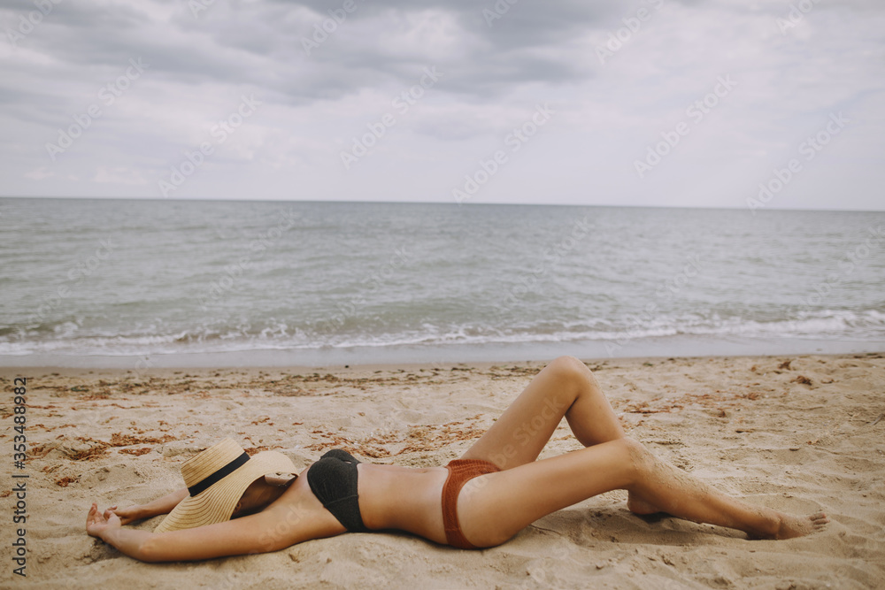 Summer vacation and travel. Girl lying on beach with hand holding hat. Fashionable young woman in straw hat relaxing on sandy beach near sea. Carefree. Top view Summer vacation and travel. Girl lying on beach with hand holding hat. Fashionable young woman in straw hat relaxing on sandy beach near sea. Carefree. Top view