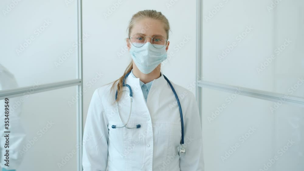 Slow motion of female doctor young blonde standing in white suit and facial mask against white background and looking at camera. People and healthcare concept. Slow motion of female doctor young blonde standing in white suit and facial mask against white background and looking at camera. People and healthcare concept.