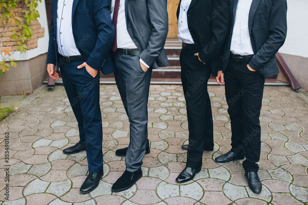 A company of stylish men in expensive suits stands with his hands in his pockets in nature. Wedding party of friends and groom. Advertising models. Photography, concept. A company of stylish men in expensive suits stands with his hands in his pockets in nature. Wedding party of friends and groom. Advertising models. Photography, concept.