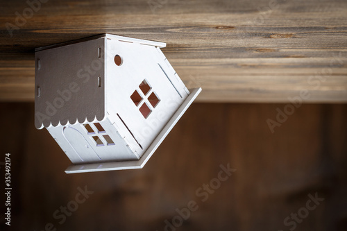 White model of a house staning on a triangle roof upside down  on a brown wooden background