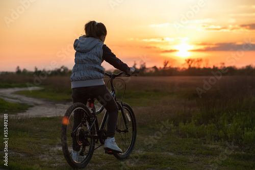 A teenage girl stopped to watch a beautiful sunset in a field. A walk on the bike . Active lifestyle.