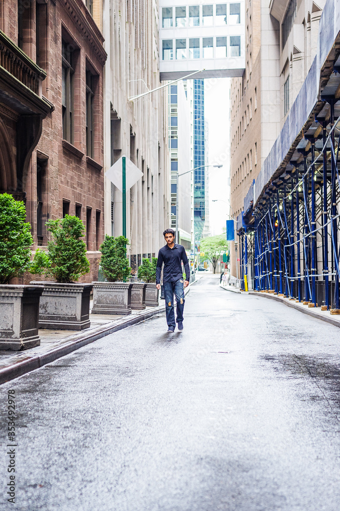 Raining day - wet, drizzle, grainy feel. Lonely East Indian American teenager wearing black long sleeve shirt,  broken fashionable jeans, cloth shoe, walking on narrow street in New York City..