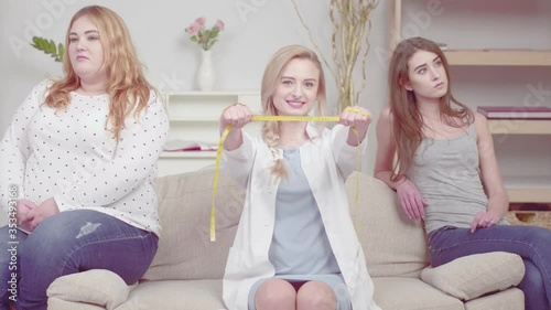 Nutritionist showing measuring string and blink while girls with a weight problem are sitting next to a nutritionist and looking upset to the sides. Proper nutrition concept. Prores 422. 
