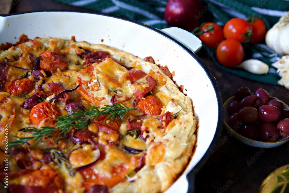 Pan pizza with tomato, olives, pancetta. Cherry tomatoes, a bowl of olives and a bulb of garlic enter the frame Pan pizza with tomato, olives, pancetta. Cherry tomatoes, a bowl of olives and a bulb of garlic enter the frame