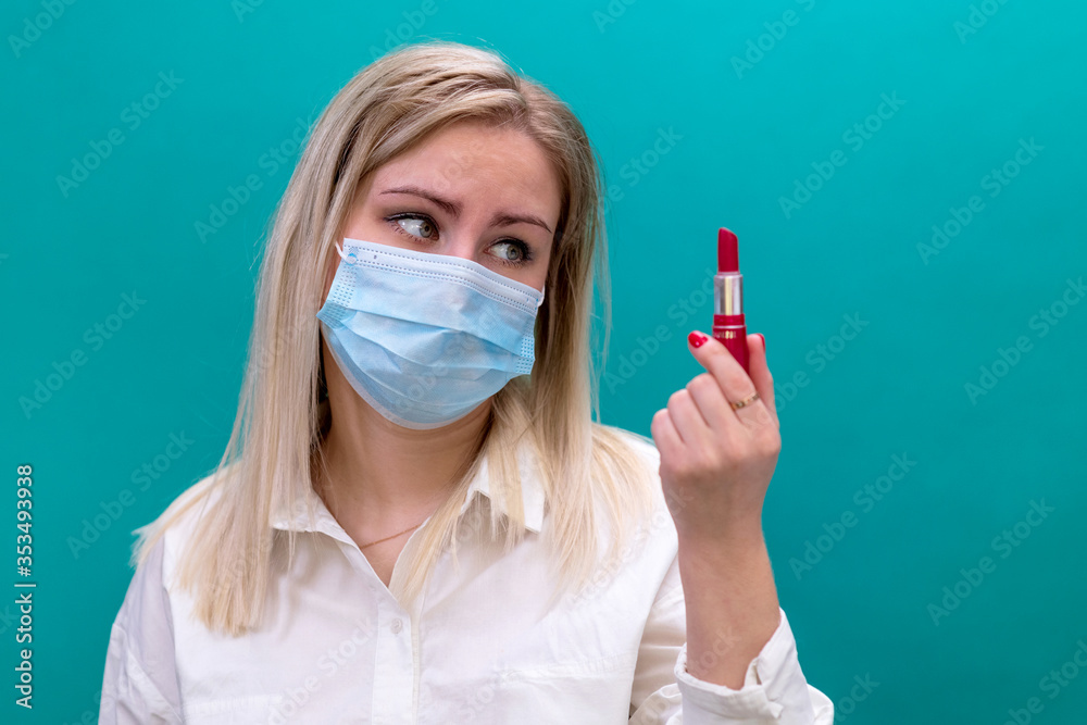 A woman in a protective medical face mask holds lipstick in her hand. Use of cosmetics during the COVID-19 coronavirus pandemic. Selective focus. A woman in a protective medical face mask holds lipstick in her hand. Use of cosmetics during the COVID-19 coronavirus pandemic. Selective focus.