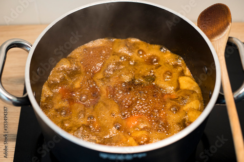 Apricot jam preparation in a black pot. Fruit preserve boiling in a big casserole with a wooden spoon. 