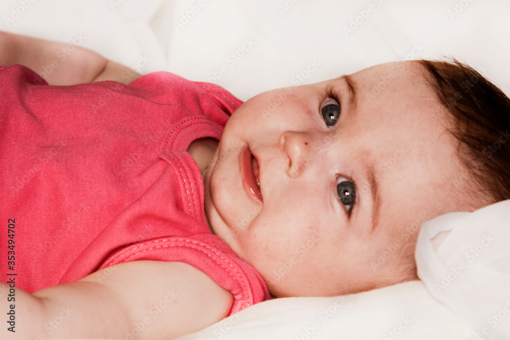 Carefree baby with a smile on his face close-up. Baby on a light background close-up. Playing little child portrait photo. Happy baby lies on the bed Carefree baby with a smile on his face close-up. Baby on a light background close-up. Playing little child portrait photo. Happy baby lies on the bed