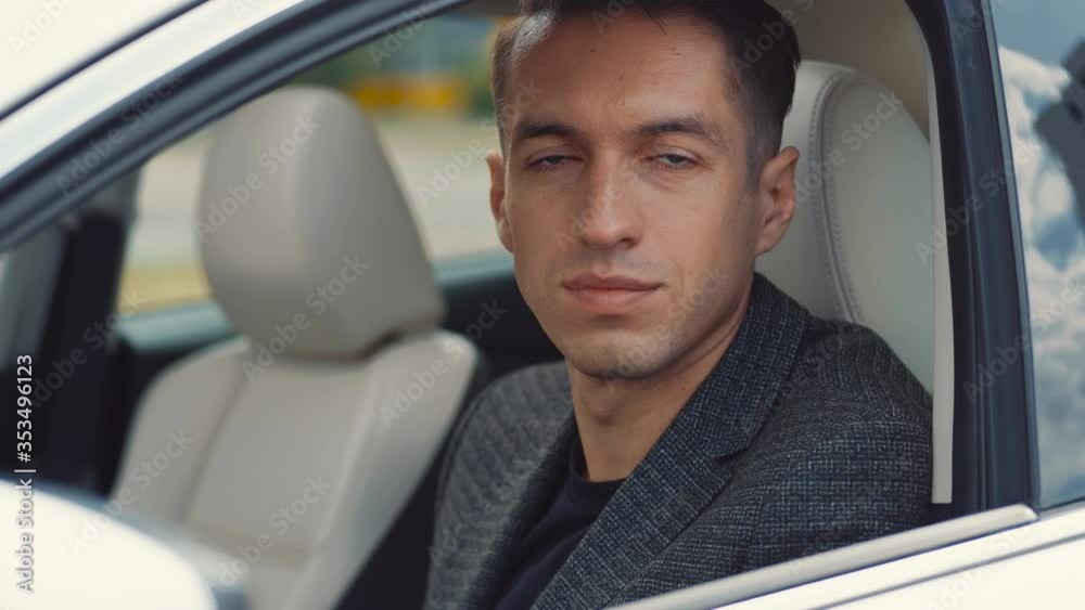 Portrait of confident male entrepreneur sitting in a car at a driver's seat and looking at the camera. Young caucasian businessman roll the window down, of a car. Portrait of confident male entrepreneur sitting in a car at a driver's seat and looking at the camera. Young caucasian businessman roll the window down, of a car.