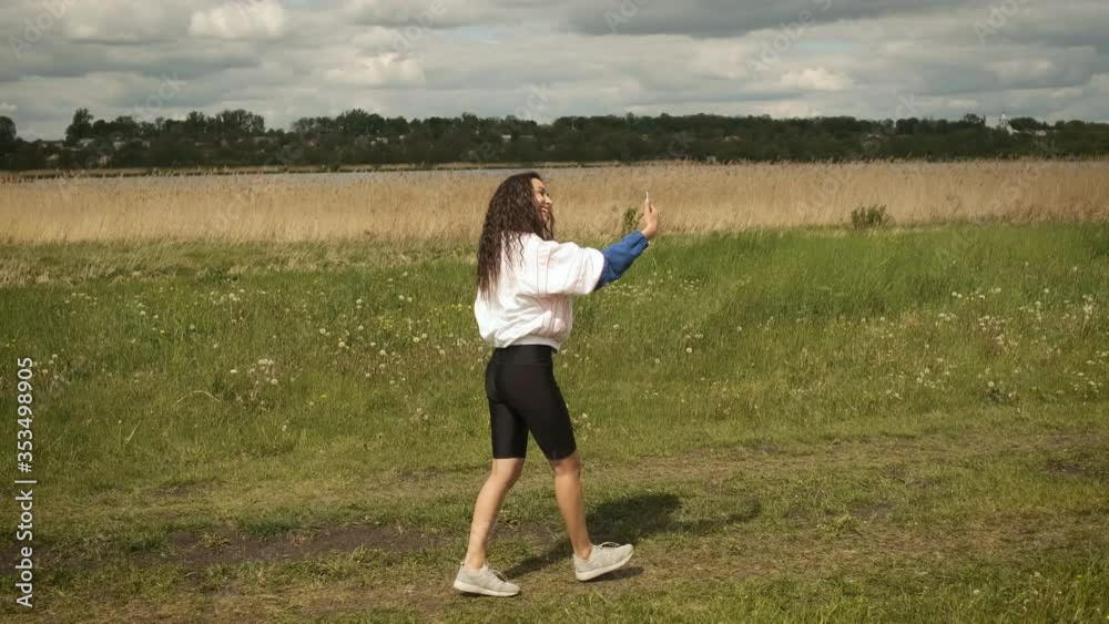 Beautiful happy smiling girl walks in the park on the background of the lake communicates through a video call on a smartphone Beautiful happy smiling girl walks in the park on the background of the lake communicates through a video call on a smartphone