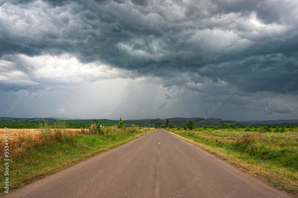 Road to dramatic storm scene with rain at the horizon. Dark sky and dramatic black cloud.
