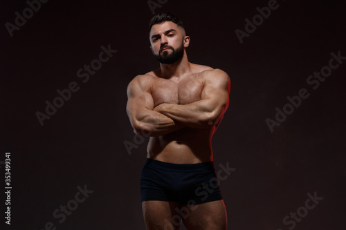 Portrait of a young bearded athletic man with a naked muscular torso with arms crossed on his chest. Isolated against a dark background.