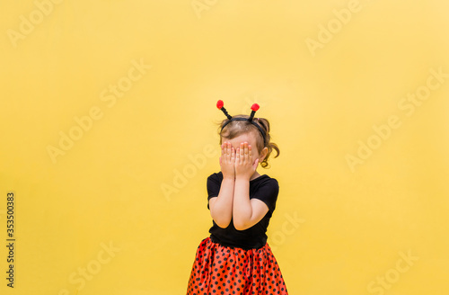 Portrait of a little girl in a ladybug costume closed her eyes on a yellow isolated background with space for text.