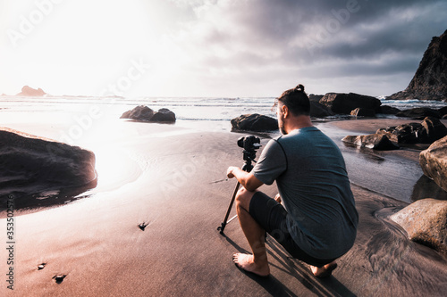 Male photographer with his camera and tripod adjusting the parameters to take a photograph at sunset on the beach of Benijo