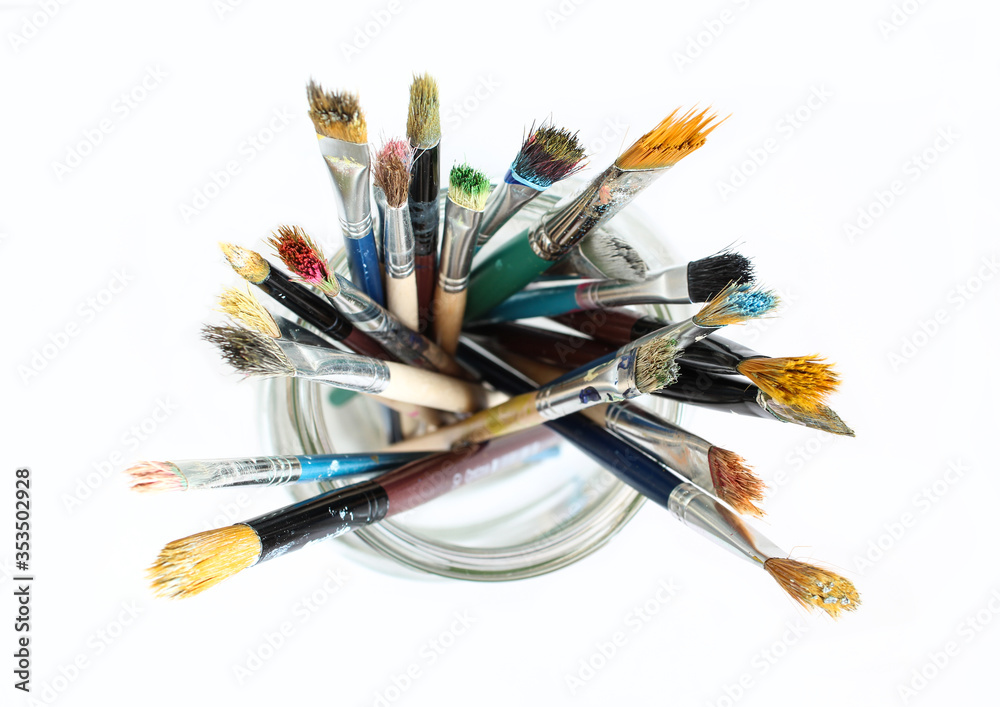 Obraz premium Bunch of dirty used paint brushes in glass. Colorful drawing accessory. Above view