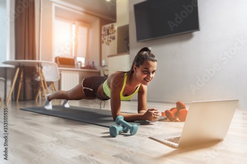 Young caucasian woman making a plank exersise at home via internet. Online training concept.