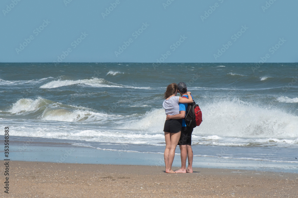 A young couple embrace while watching the ocean waves. A young couple embrace while watching the ocean waves.