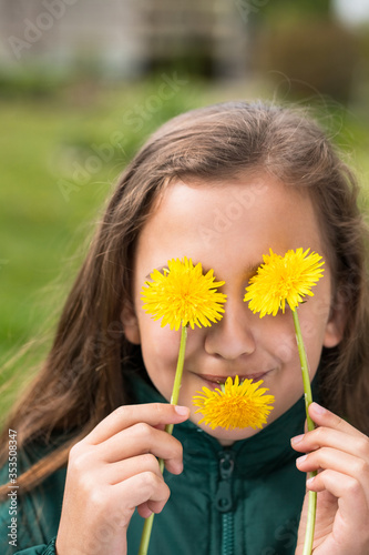 Little Girl With Dandelions In Hands Near Eyes And In Mouth In Garden Close-Up.