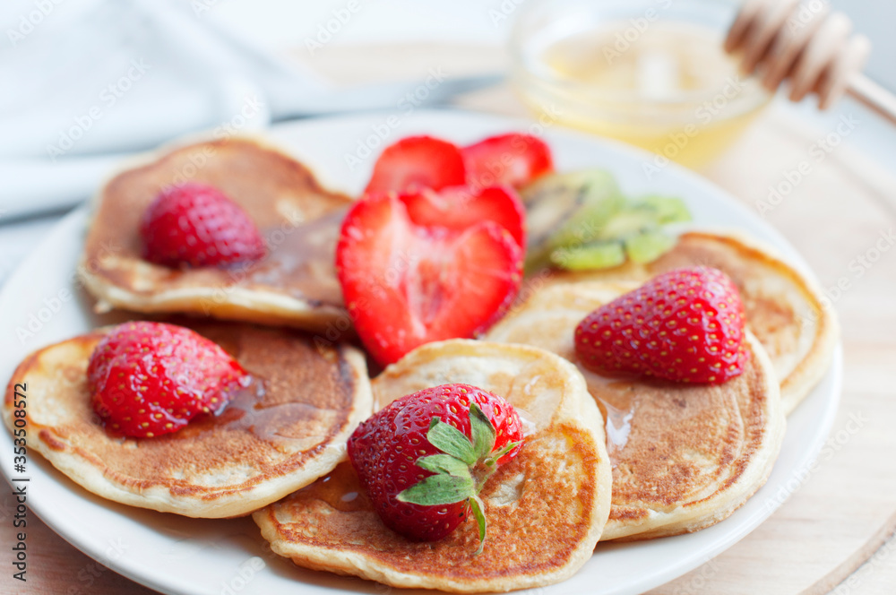 Breakfast with pancakes with strawberry, kiwi and honey on white background. Tasty breakfast for child on wooden board Breakfast with pancakes with strawberry, kiwi and honey on white background. Tasty breakfast for child on wooden board