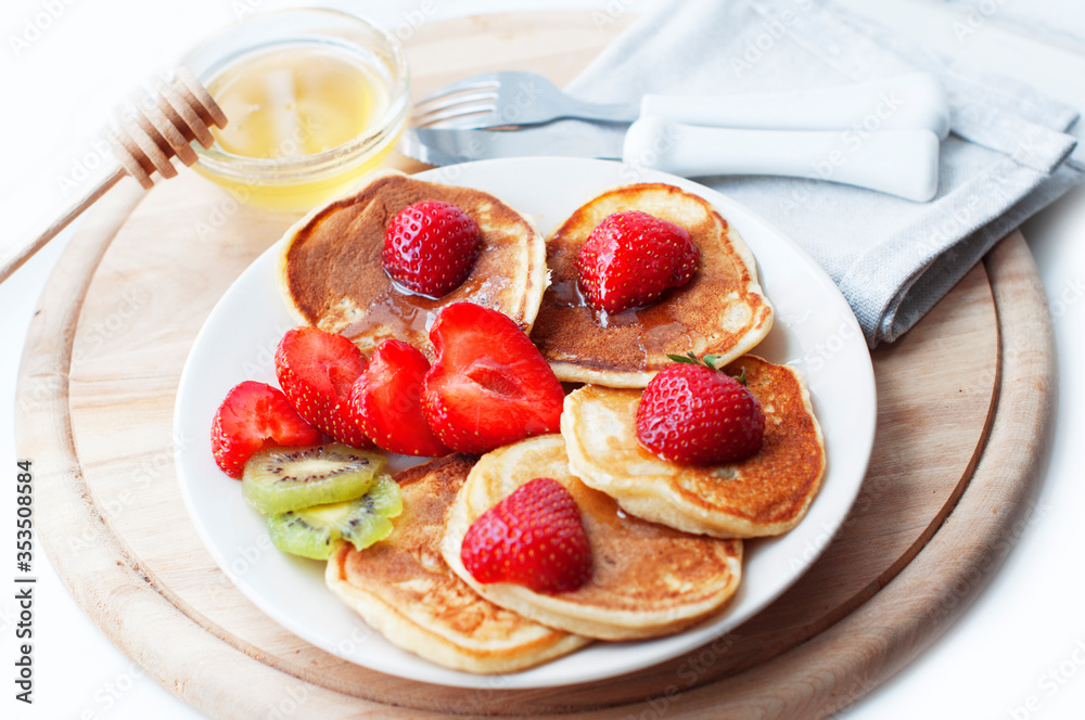 Breakfast with pancakes with strawberry, kiwi and honey on white background. Tasty breakfast for child on wooden board Breakfast with pancakes with strawberry, kiwi and honey on white background. Tasty breakfast for child on wooden board