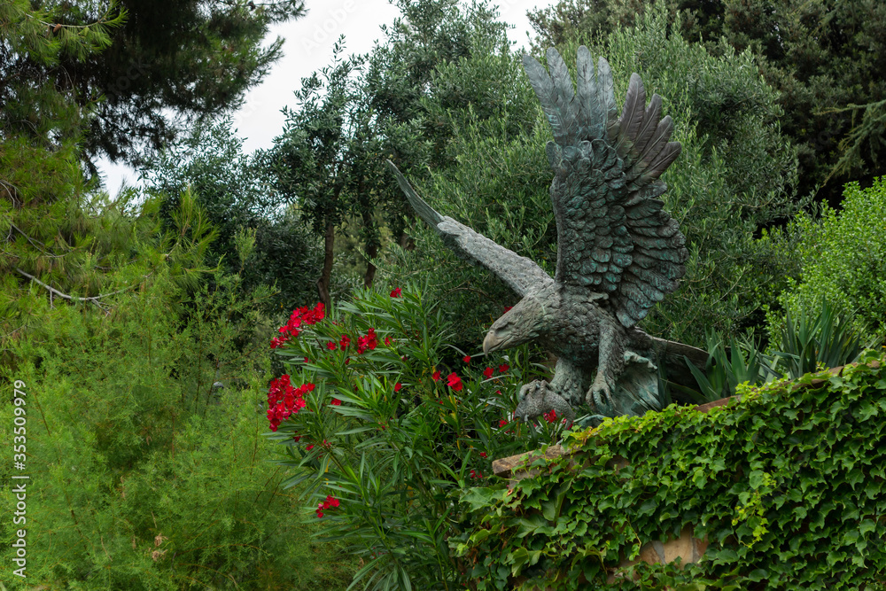 Alushta, Russia - July 29, 2016: Bronze eagle in the Aivazovsky landscape park in Partenit in Crimea among flowering shrubs.