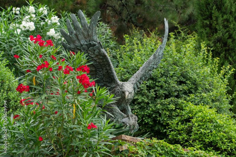 Alushta, Russia - July 29, 2016: Bronze eagle in the Aivazovsky landscape park in Partenit in Crimea among flowering shrubs.