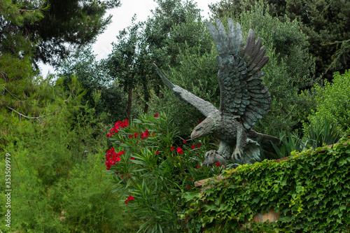 Obraz na płótnie Alushta, Russia - July 29, 2016: Bronze eagle in the Aivazovsky landscape park in Partenit in Crimea among flowering shrubs. w salonie