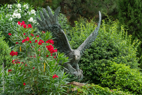 Obraz na płótnie Alushta, Russia - July 29, 2016: Bronze eagle in the Aivazovsky landscape park in Partenit in Crimea among flowering shrubs. w salonie