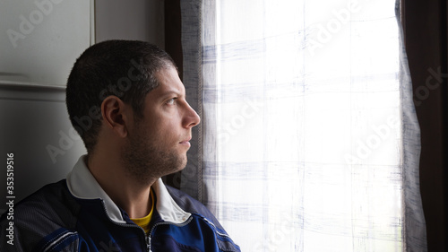 Angle view of a young and short hair guy looking sad at the window