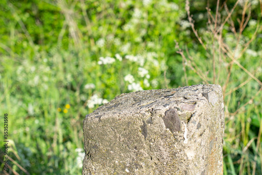 Standing old gray concrete pillar with planar surface on the top as a stage for something and blurred green grass background behind. Standing old gray concrete pillar with planar surface on the top as a stage for something and blurred green grass background behind.