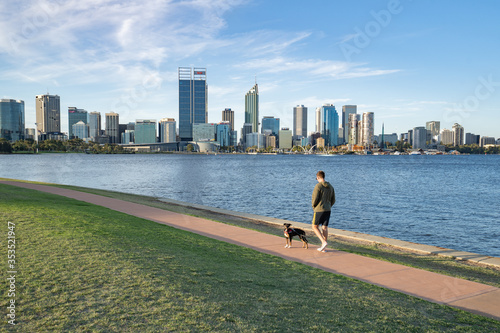 Man walking his dog along the South Perth Foreshore at sunrise. The beautiful Perth city is in the background. 