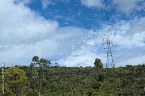 Vibrant capture of an energy tower with high voltage cables line at the top of a forest mountain and blue cloudy sky at background. Energy and environment care concept