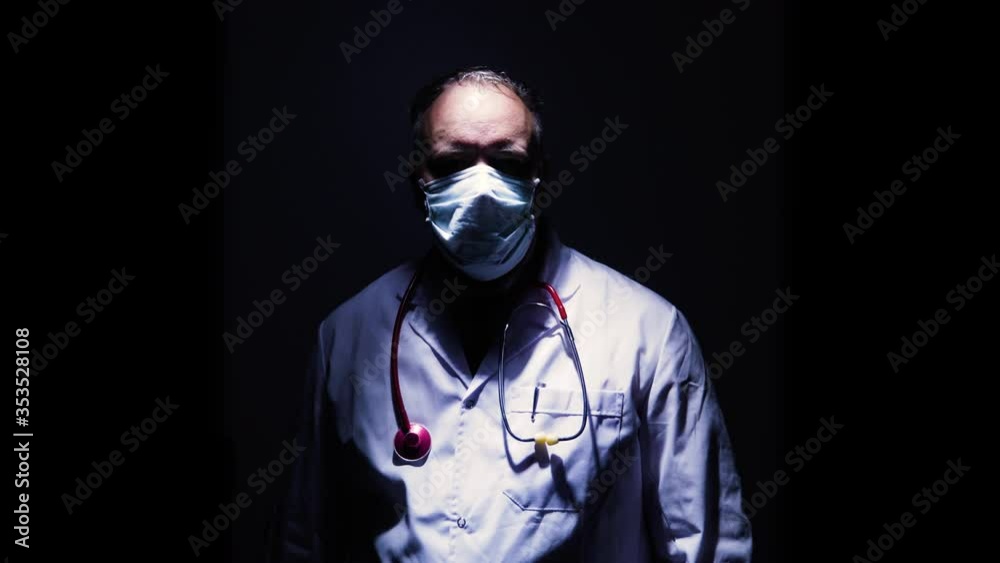 Portrait of doctor with face mask and gloves coming from dark then stares into camera with a hard shadow He is a hero like nurses doctor virologist who fight against coronavirus COVID 19 in Quarantine Portrait of doctor with face mask and gloves coming from dark then stares into camera with a hard shadow He is a hero like nurses doctor virologist who fight against coronavirus COVID 19 in Quarantine