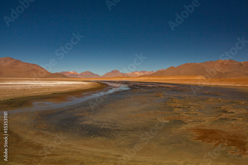 Colorful Lake Hosting Flamingos Surrounded by Salt Patches and Orange Mountain Ranges