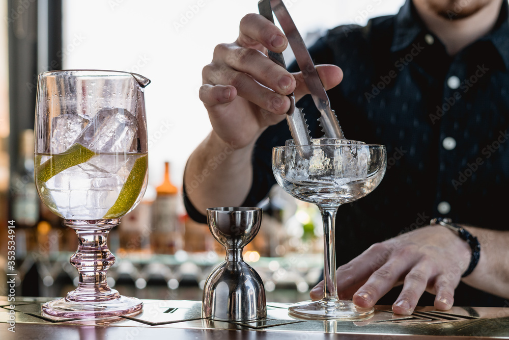 Copa de cocktails en un bar con cubo de hielo puesto con pinzas de coctelería con jigger