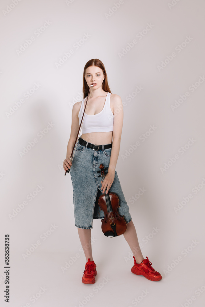 The girl in jeans and red sneakers plays the violin on a white background The girl in jeans and red sneakers plays the violin on a white background