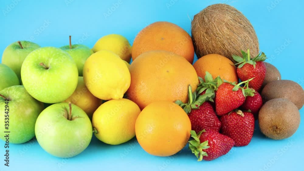 Pile of different fresh organic fruits on blue background. Oranges, apples, kiwi, strawberries, lemons and coconut Pile of different fresh organic fruits on blue background. Oranges, apples, kiwi, strawberries, lemons and coconut