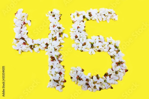 Obraz na płótnie The number 45 is written in white acacia flowers on a yellow background. The number forty five is written in fresh colors, isolated on yellow. Arabic numeral lined with flowers. w salonie