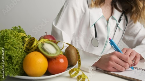 Female doctor nutritionist in a medical gown sits at work and prescribes a healthy diet photo