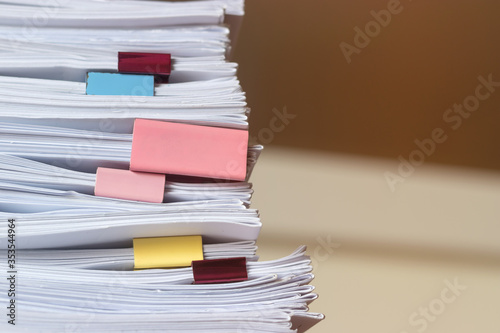 Pile of student homework that assigned to student to be completed outside class on teacher desk separated by colored paper clips. Document stack arranged by paperclip. Business and education concept.