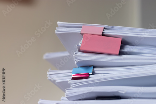 Pile of student homework that assigned to student to be completed outside class on teacher desk separated by colored paper clips. Document stack arranged by paperclip. Business and education concept.