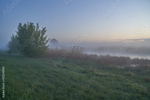 Early spring. Morning dawn over the lake in a misty, thoughtful haze. Beautiful view of the forest covered with fog early in the morning. The sun's rays of light. May.