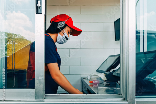Bangkok, Thailand - May 28, 2020 : fast food cashier in drive thru service wearing hygiene face mask to protect coronavirus pandemic or covid-19 virus outbreak working on counter at the station. photo