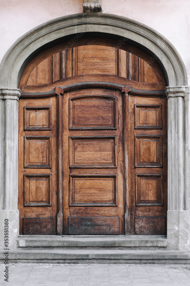 Old wooden brown door. Facade of gray stone with portal. Old wooden brown door. Facade of gray stone with portal.