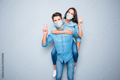 Smiling happy boyfriend carry piggy back his girlfriend gesturing v-sign wear medical safety sterile mask on face, pandemic corona virus prevention protection trend fashion concept 2020 covid19 photo