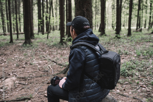 Traveler man relaxing in forest with photo camera, backpack. Travel lifestyle concept vacations outdoor.