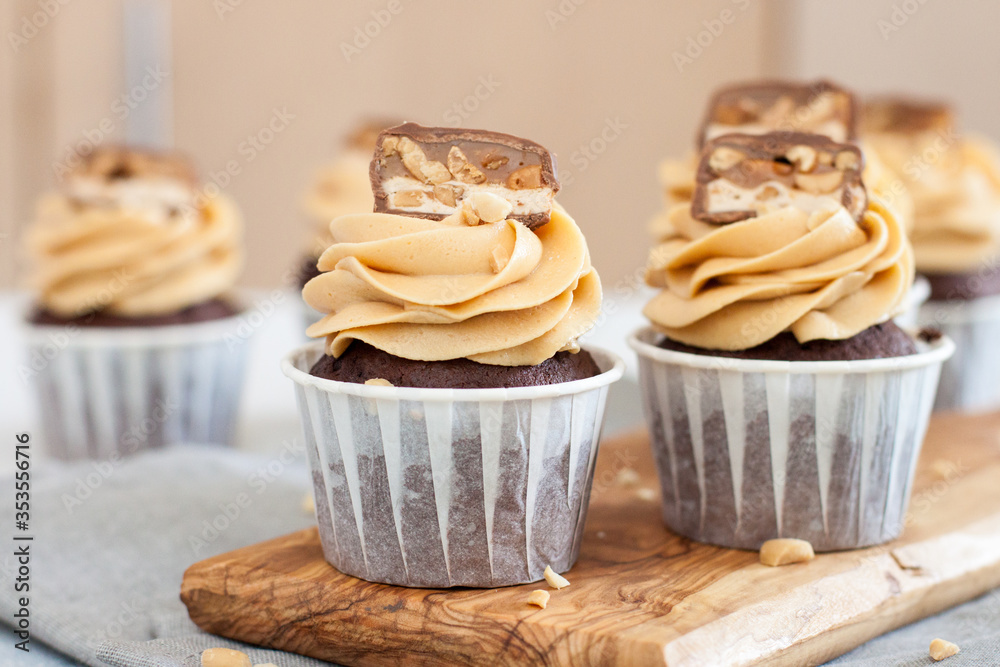Peanut butter cupcakes with chocolate bites and chopped nuts on grey linen tablecloth.