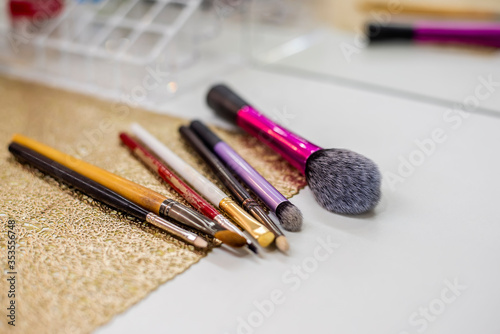 On a gold glitter sheet lie different shapes and sizes of brushes for professional makeup. Designed for applying foundation, eye shadow, powder, lips, cheekbone face correction. Selective soft focus