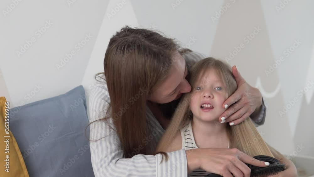 A woman combs her little daughter's hair in the morning in the nursery. A woman combs her little daughter's hair in the morning in the nursery.